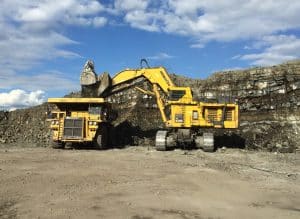 Image of a Komatsu excavator pouring debris into a mechanical haul truck. Image highlights the fact that Roadwarrior emissions part D2048-FL is an exact-fit replacement for Komatsu DOC and DPF combination C6527-01-0010.